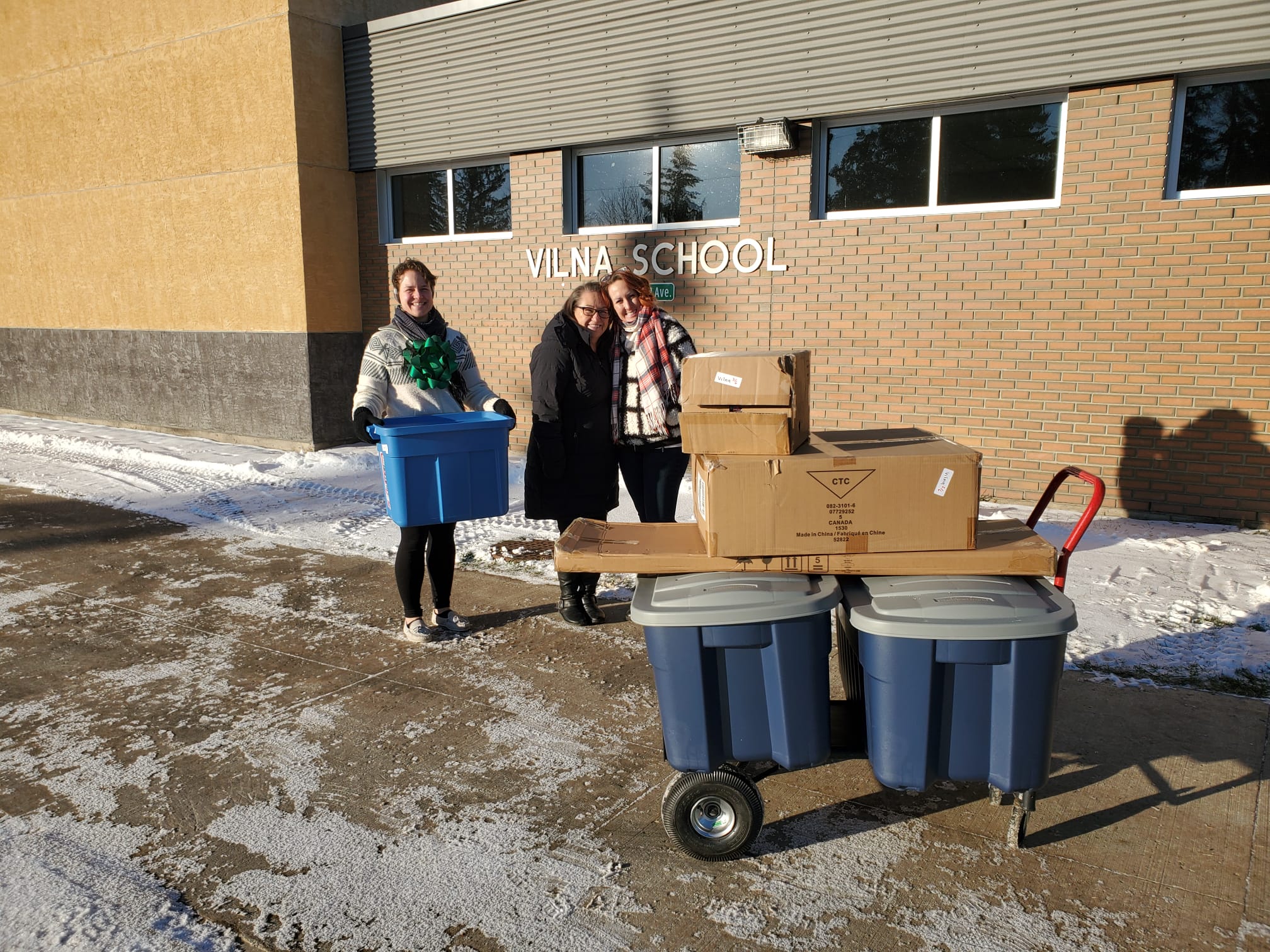 Three women stand outside Vilna school with packages from Canadian Tire Jumpstart